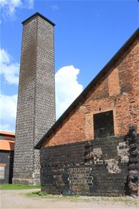 An older industrial building in red and black brick, a high gray brick chimney on the left.