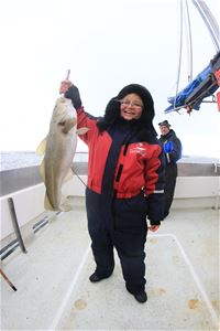 Bildet viser en dame som holder opp en stor torsk hun har fått på kroken
