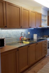 Köksskåp med yta av trä, blått kakel, diskbänk, diskställ och en spis. 