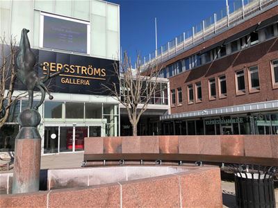 In the foreground a fountain, a white building with a black sign with text in golden letters Bergströms galleria.