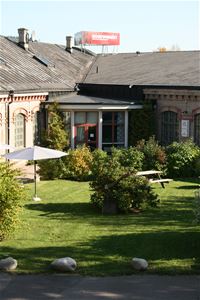 En innergård med gräsmatta , i bakgrunden en stor  industribyggnad med en röd skylt på taket Biografmuseet.