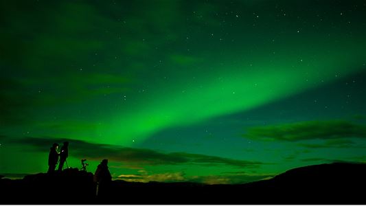 Gruppe med gjester ser på kraftig nordlys under en nordlystur i Tromsø-regionen.