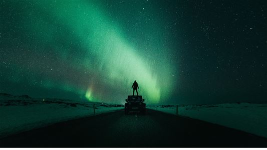 Gjest ser på nordlyset fra et mørkt vinterlandskap under en nordlysopplevelse med Legendary Adventure.