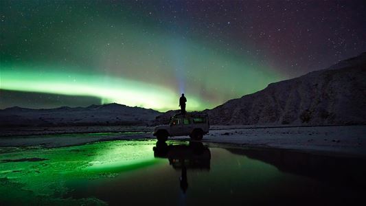 En gjest nyter utsikten over nordlyset ved en fjord omgitt av fjell.