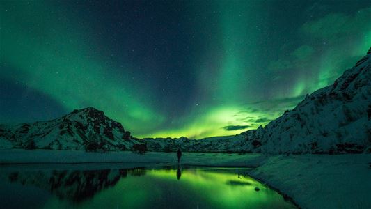 Grønt nordlys lyser opp nattehimmelen over en fjord og snødekte fjell.