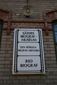 En tegelvägg med en vit skylt som ser ut som en filmrulle, text Säters biografmuseum, den rörliga bildens historia, Rio biograf.
